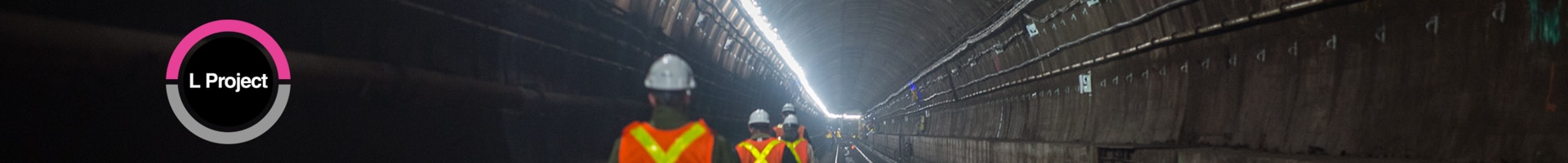 A line of workers in vests and helmets walking down a tunnel. There are two lines, one pink and one grey, that create a circle. Insider the circle is the letters L PROJECT