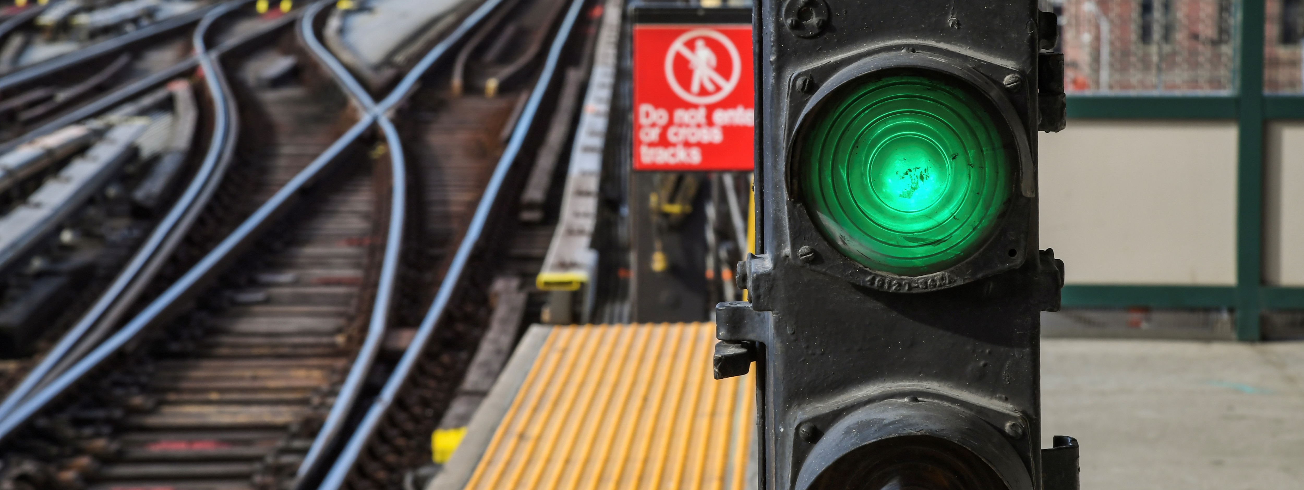 A green signal glows in the foreground of an image, with elevated subway tracks visible in the background. 