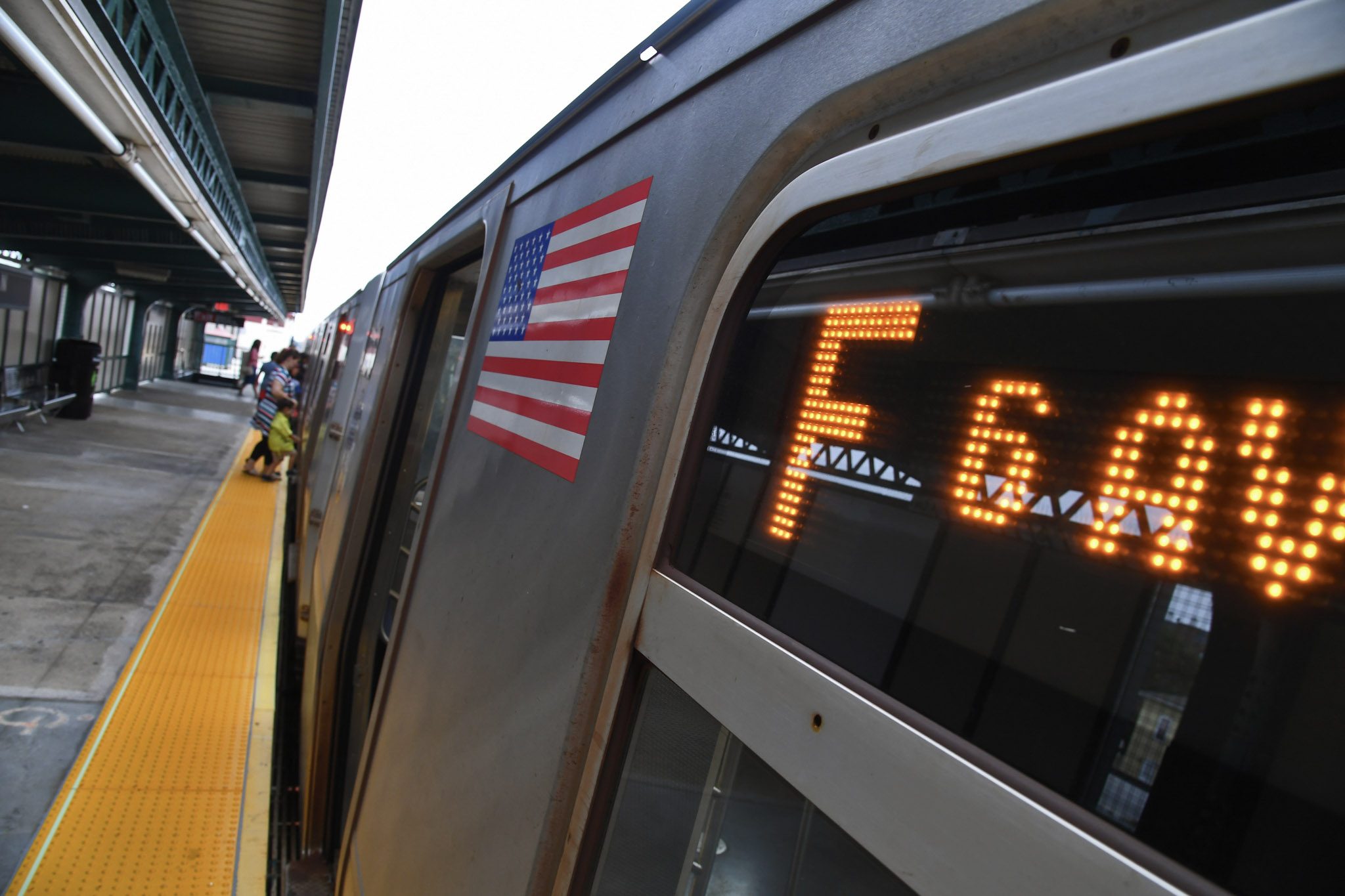 An F train stopped at a platform, with riders boarding the train.