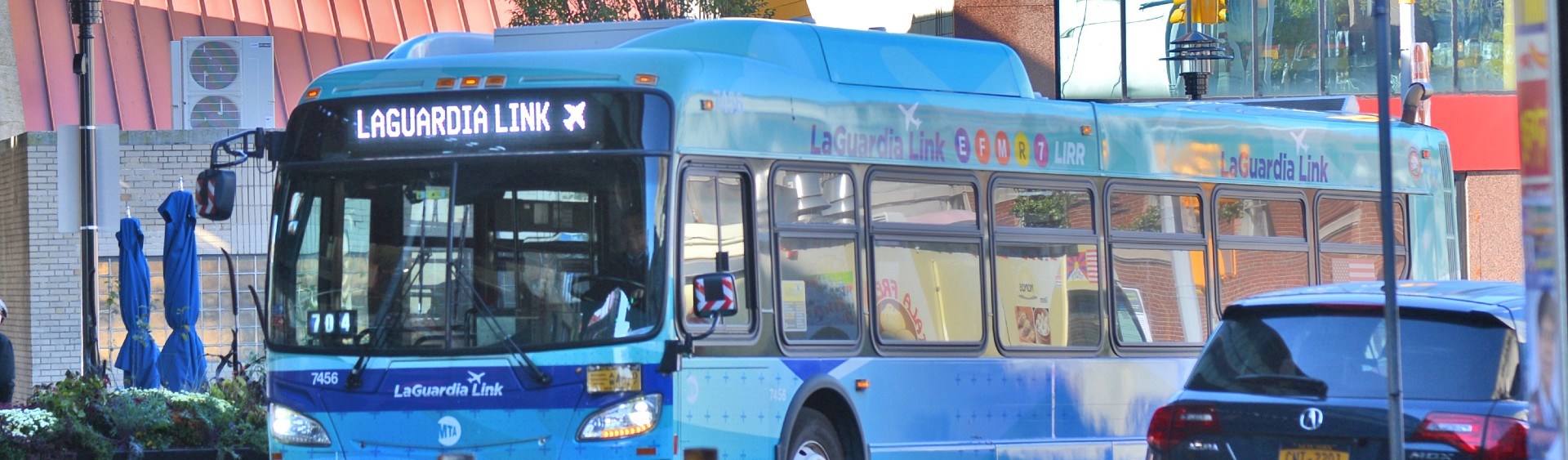 A bus traveling on a city street. A sign on the front of the bus reads "LaGuardia Link." 