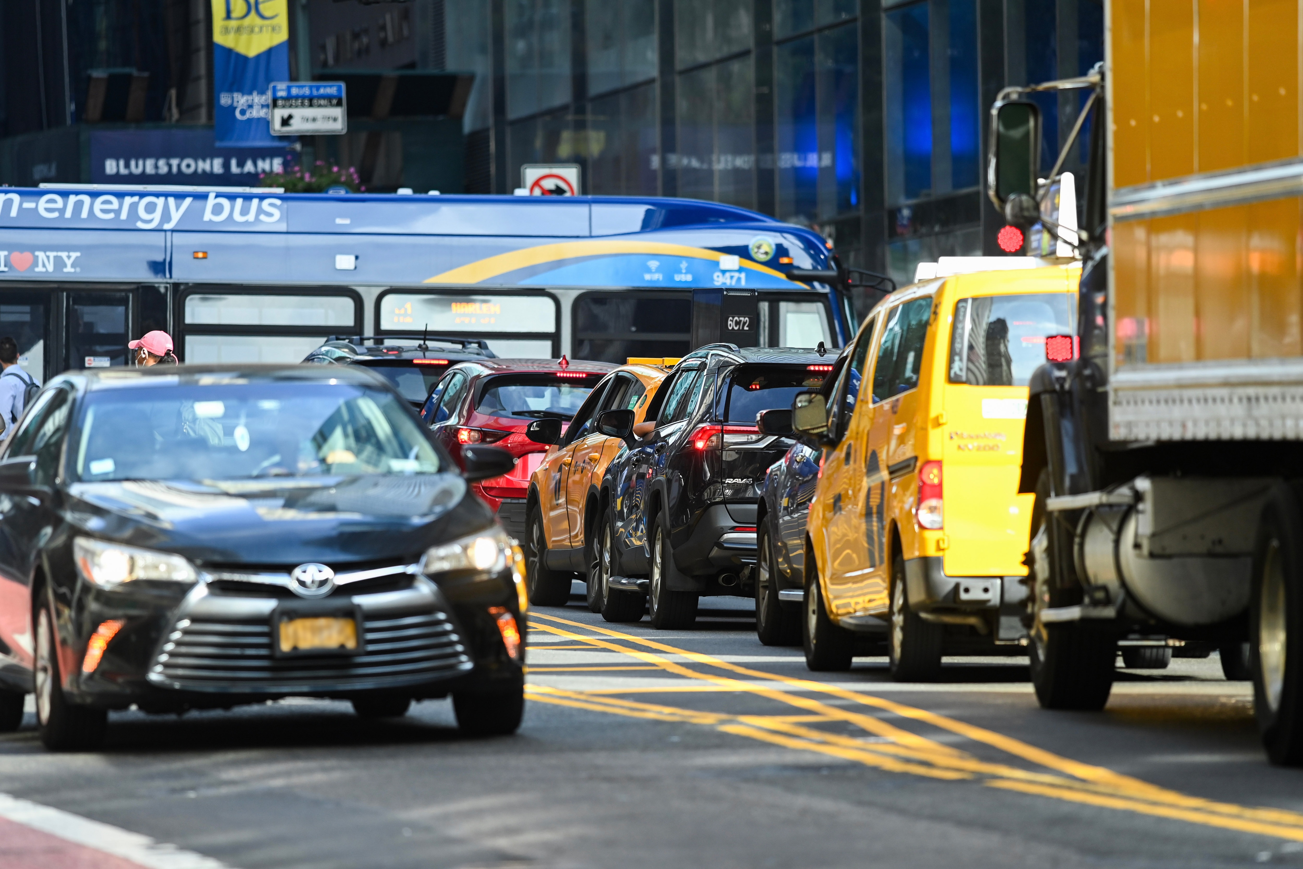 A line of cars backed up on a New York City Street while a bus crosses at the intersection