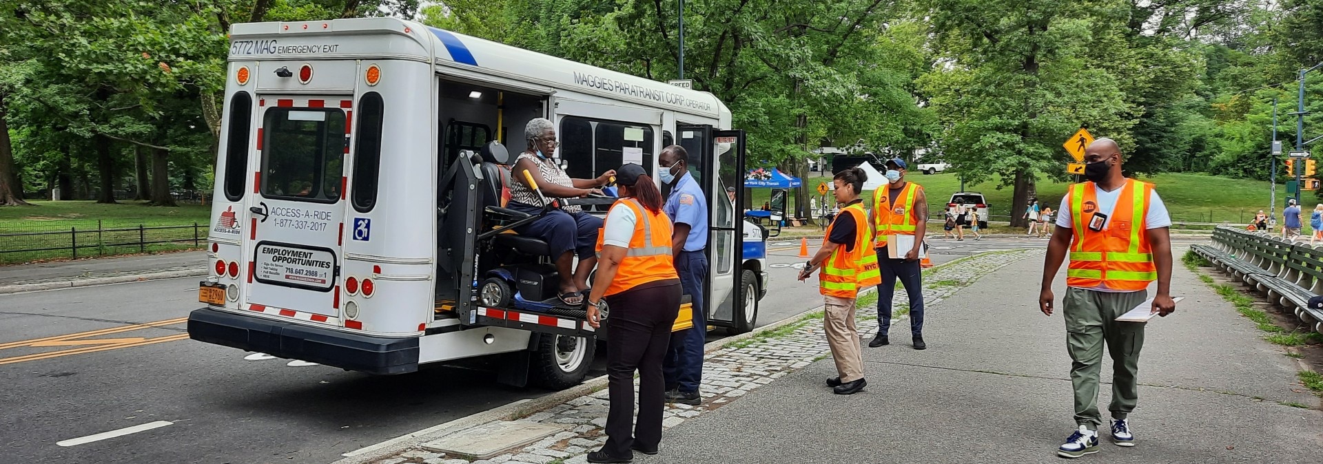 A white Access-A-Ride vehicle with workers who are helping a woman using a wheelchair. 