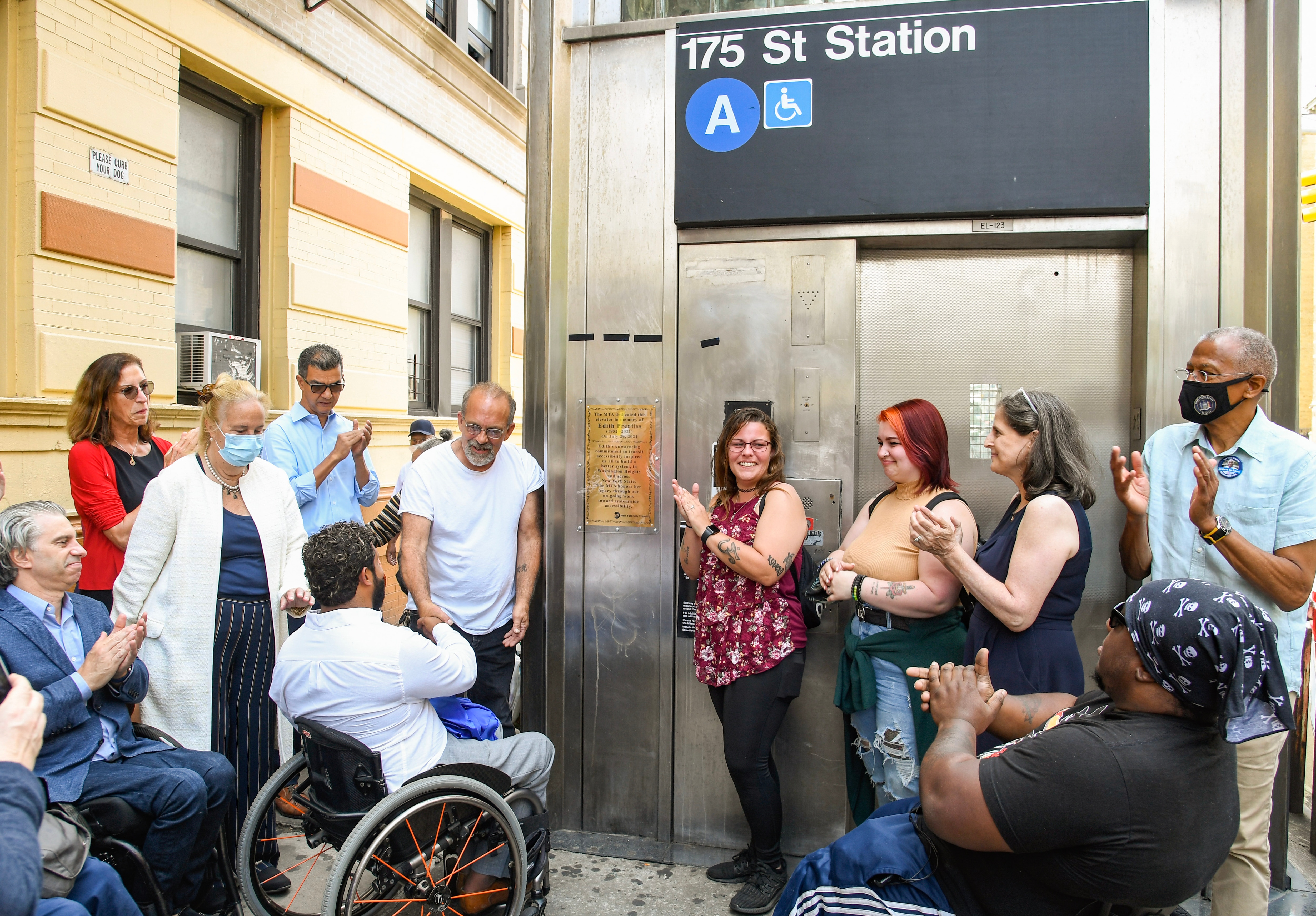 Chief Accessibility Officer Quemuel Arroyo and advocates stand around 175 Street elevator clapping as a plaque is revealed.