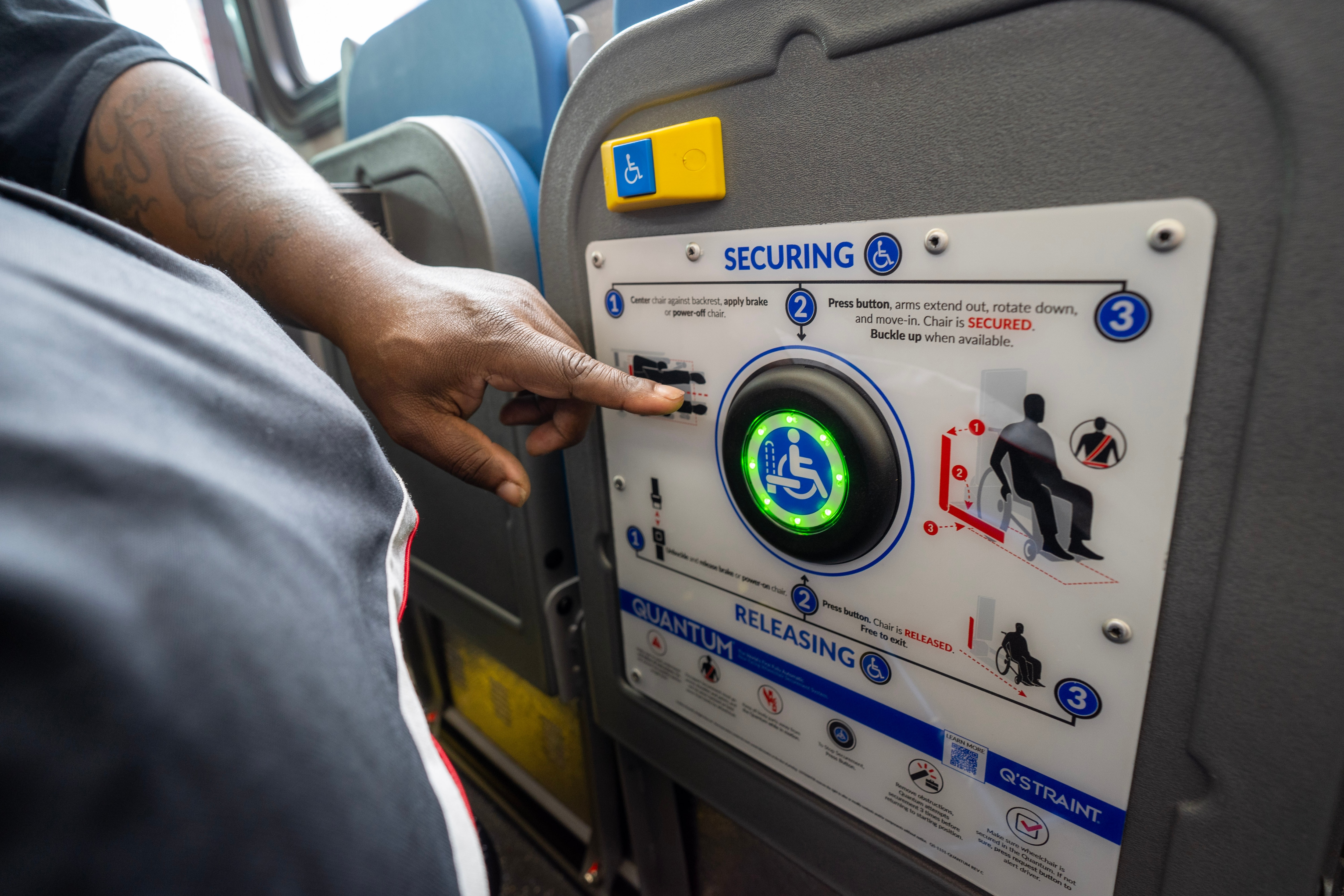 customer who uses mobility device points to button that helps secure them on a bus without the assistance of an operator 