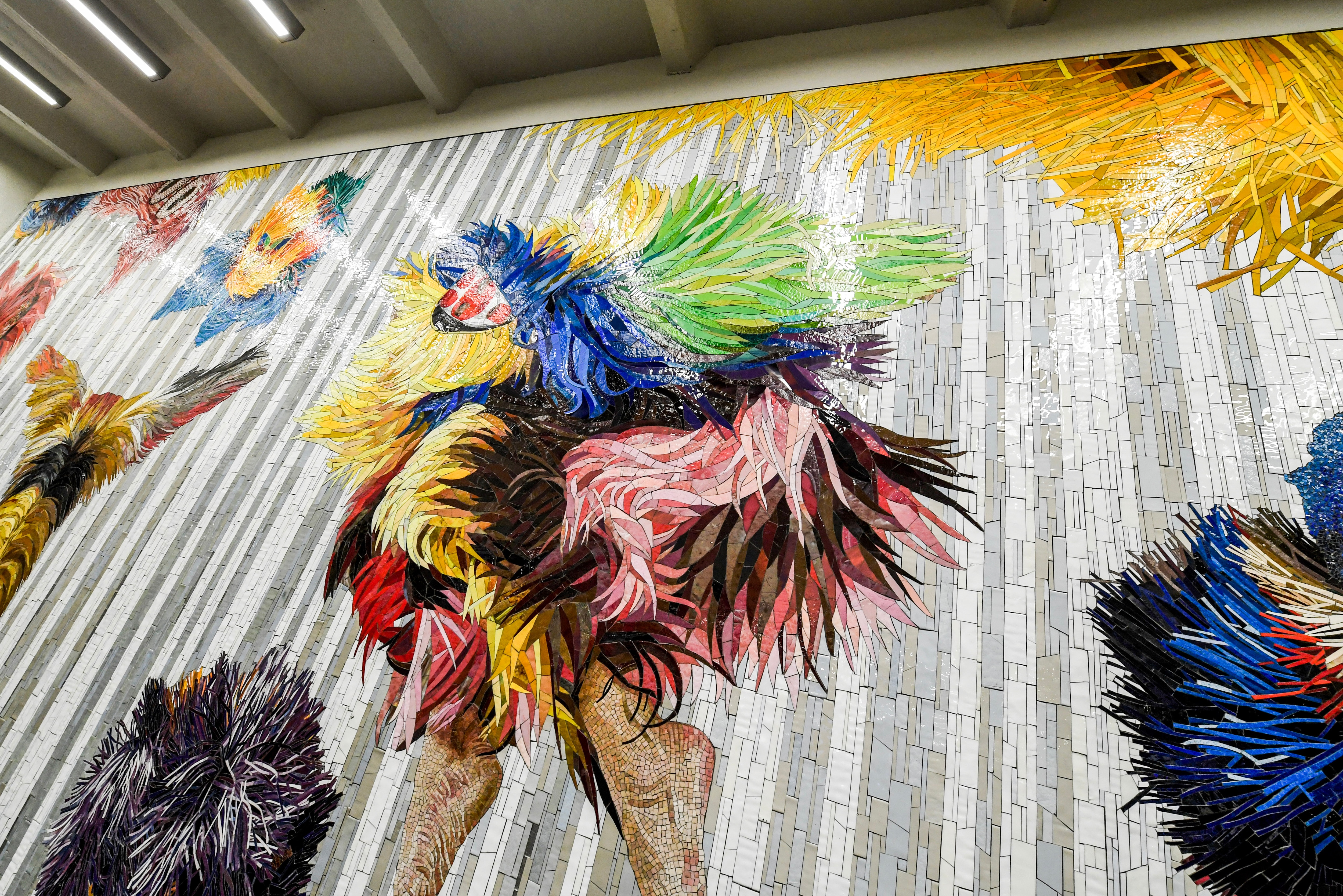 Artwork in mosaic by Nick Cave showing people dancing in brightly colored costumes known as Soundsuits