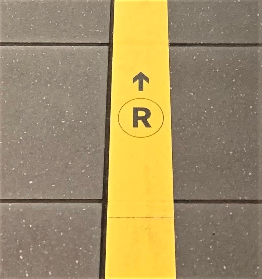 Yellow tape on station floor with R bullet and directional arrow pointing forward