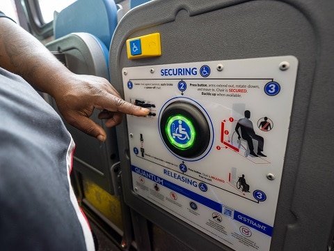 A customer reaching his hand out to push the securement signal button found on the side of the bus to start the Quantum self-securement system.