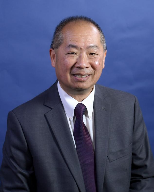 Philip Eng photographed from the chest up. He is wearing a gray suit jacket, white shirt, and purple tie.