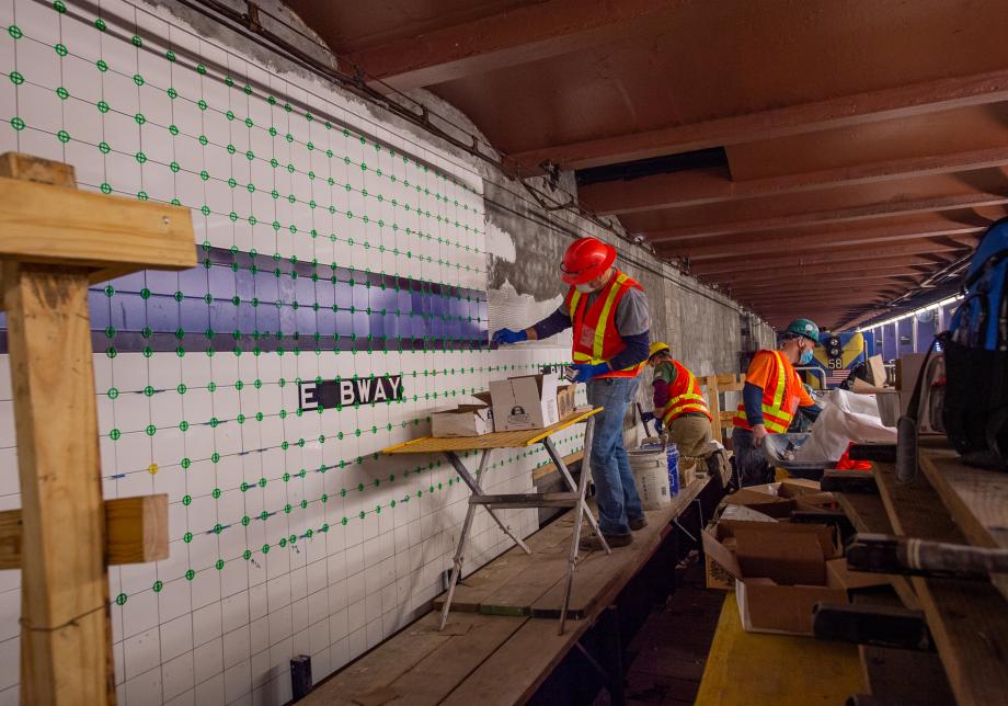 Workers place tile along the walls at the East Broadway station