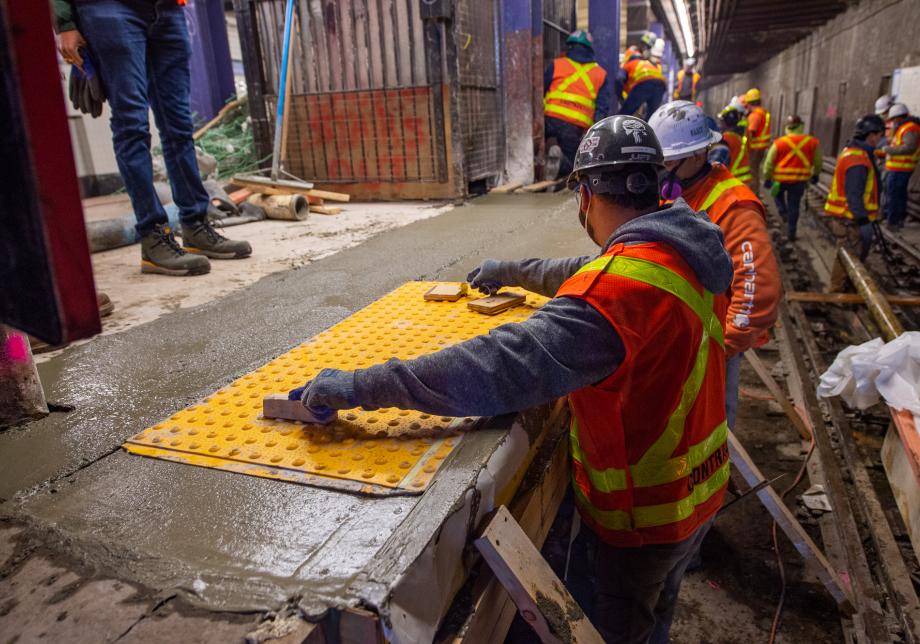 Workers place tactile strips in cement at the East Broadway station