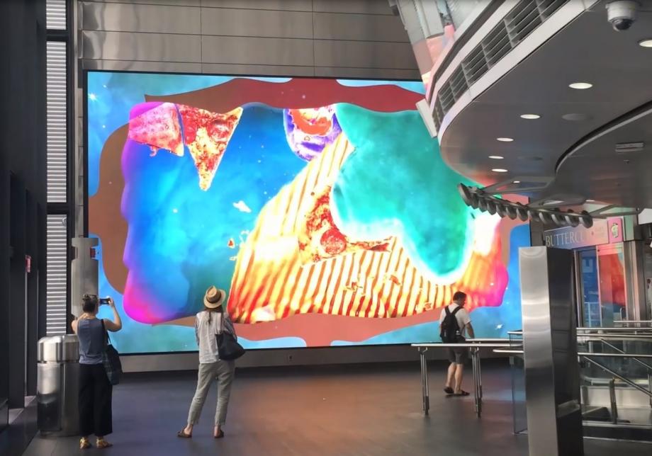 The photo shows digital artwork, Skyyys ™, created by Dave Greber at Fulton Center. Large screen displays layered objects and color on a field. 