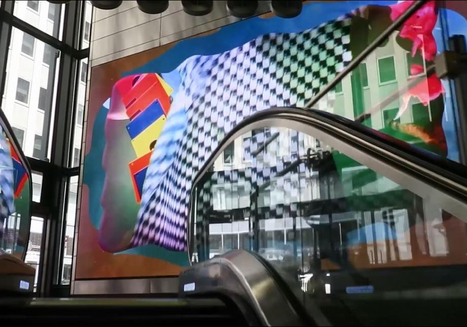 The photo shows digital artwork, Skyyys ™, created by Dave Greber at Fulton Center. Large screen displays layered objects and color on a field. 
