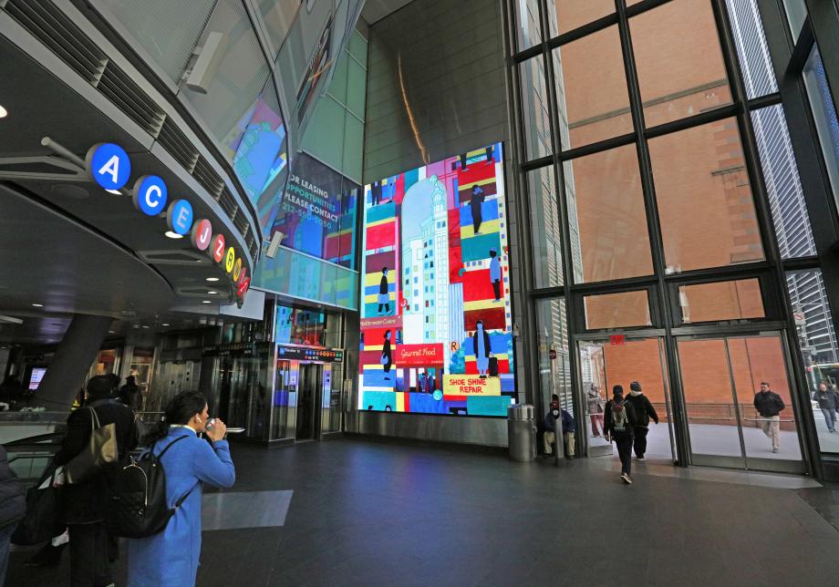 The photo shows digital artwork, Fulton Flow, created by Ezra Wube at Fulton Center. The large vertical screen shows buildings, colors and people. 