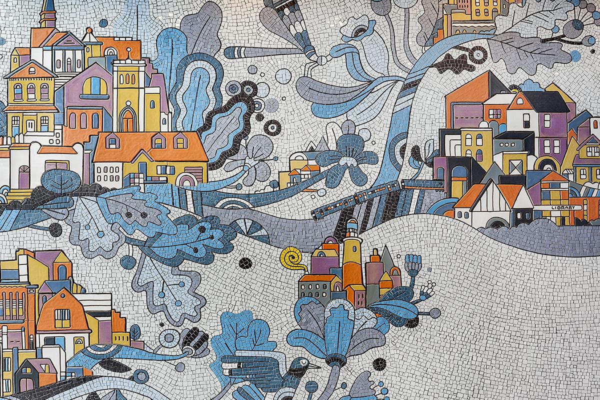 A close up view of white mosaic that features colorful buildings, branches, leaves, and flowers, a train and a lighthouse.