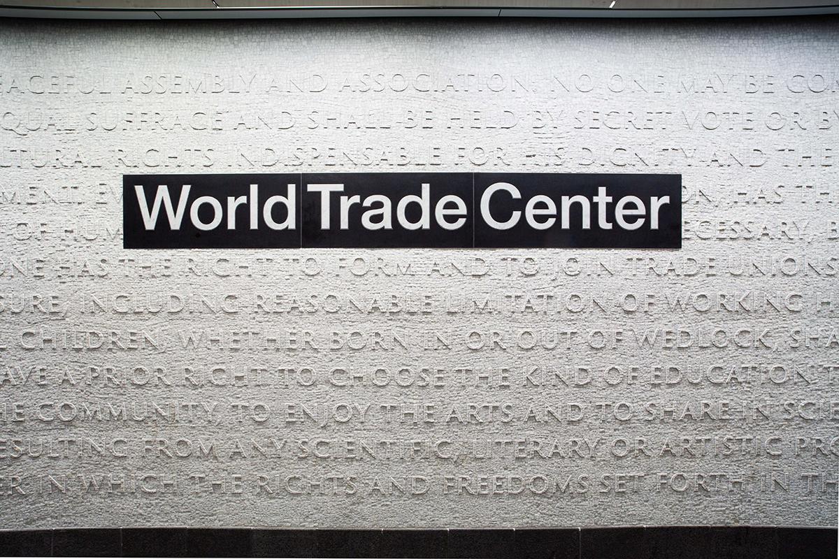 Photograph of marble mosaic artwork on the platform walls of the WTC Cortlandt station.  The white platform wall is lined with words taken from the U.S. Declaration of Independence and the 1948 United Nations Universal Declaration of Human Rights forming a monochromatic tactile surface with a large black and white station name sign sitting on the wall surface.