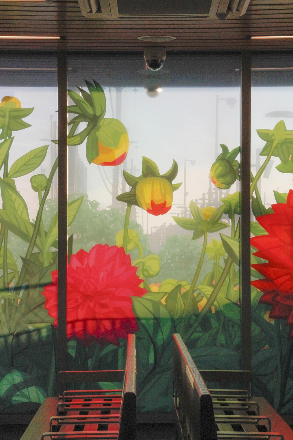Photograph of laminated glass artwork on the walls of the LIRR Deer Park station house. Photo taken from inside waiting area with light shining through large pink dahlias and tall green grass and leaves of artwork with benches in the foreground.
