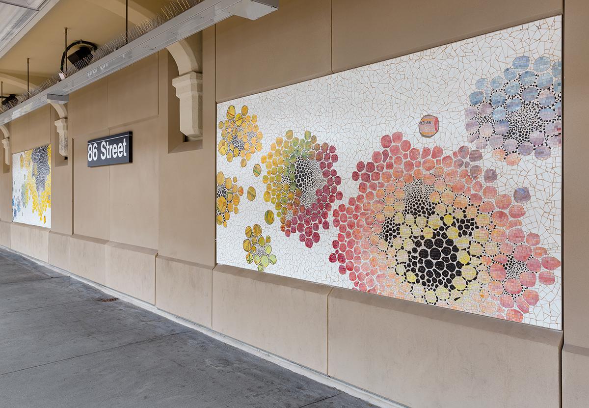 Angle view photograph of Karen Margolis mosaics on station platform wall. Mosaics are colorful circular forms on white tile background.