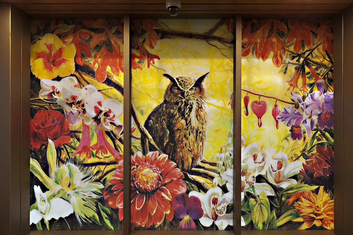 A photograph of glass artwork split in three sections. The glass artwork shows a large owl sitting amongst flowers and branches on top of a yellow background.