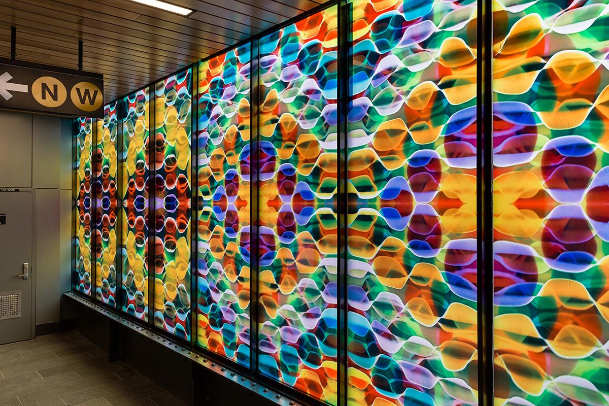 Photo of station mezzanine interior with multicolored glass artwork on right. 
