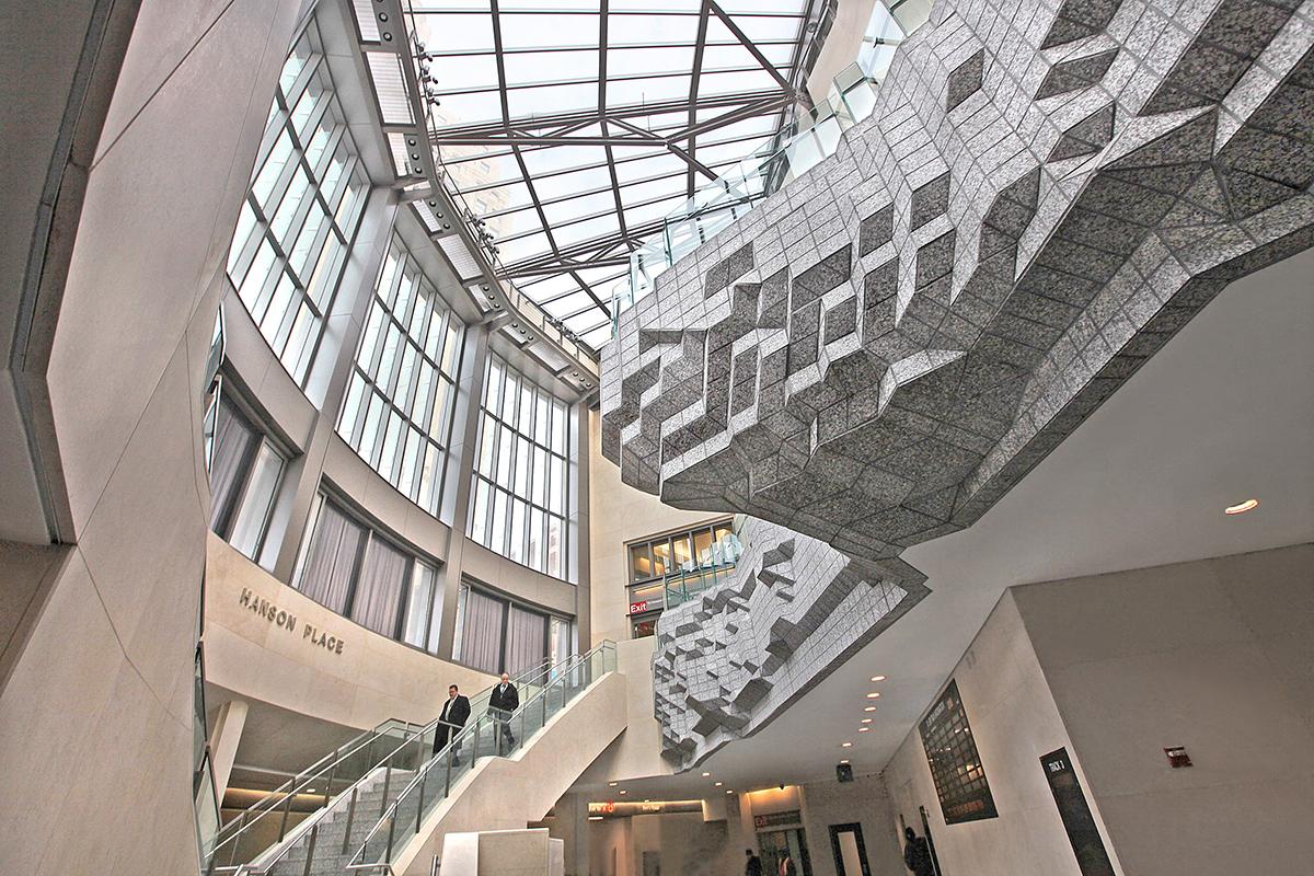Artwork in granite by Allan and Ellen Wexler showing a rocky two-story sculptural balcony framed by a pair of glass staircases. 