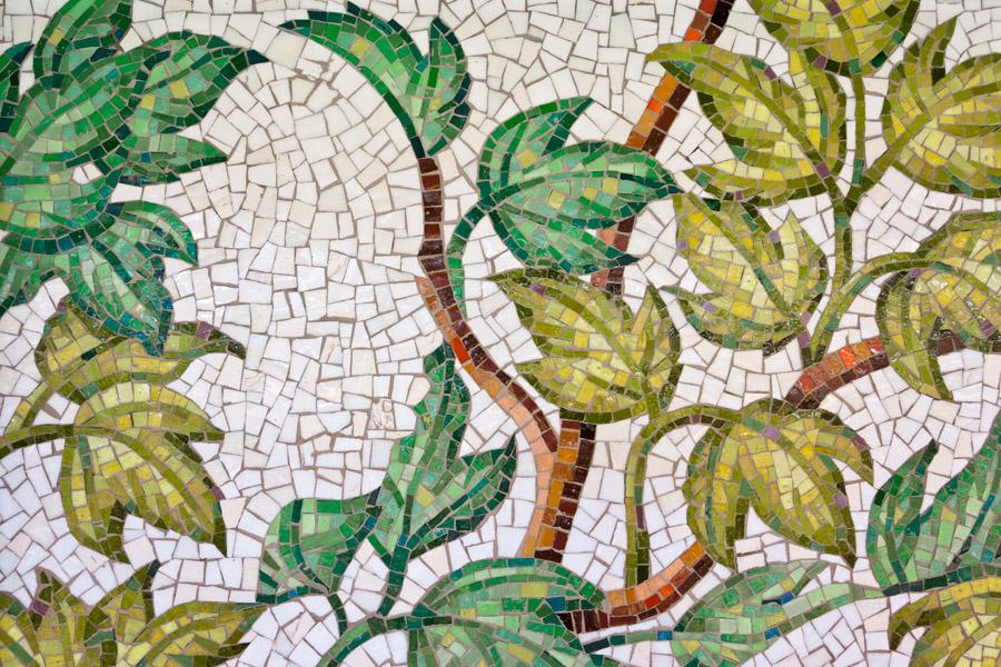 Artwork in glass mosaic by Alison Moritsugu showing a pattern of plants with silhouettes of people woven in.