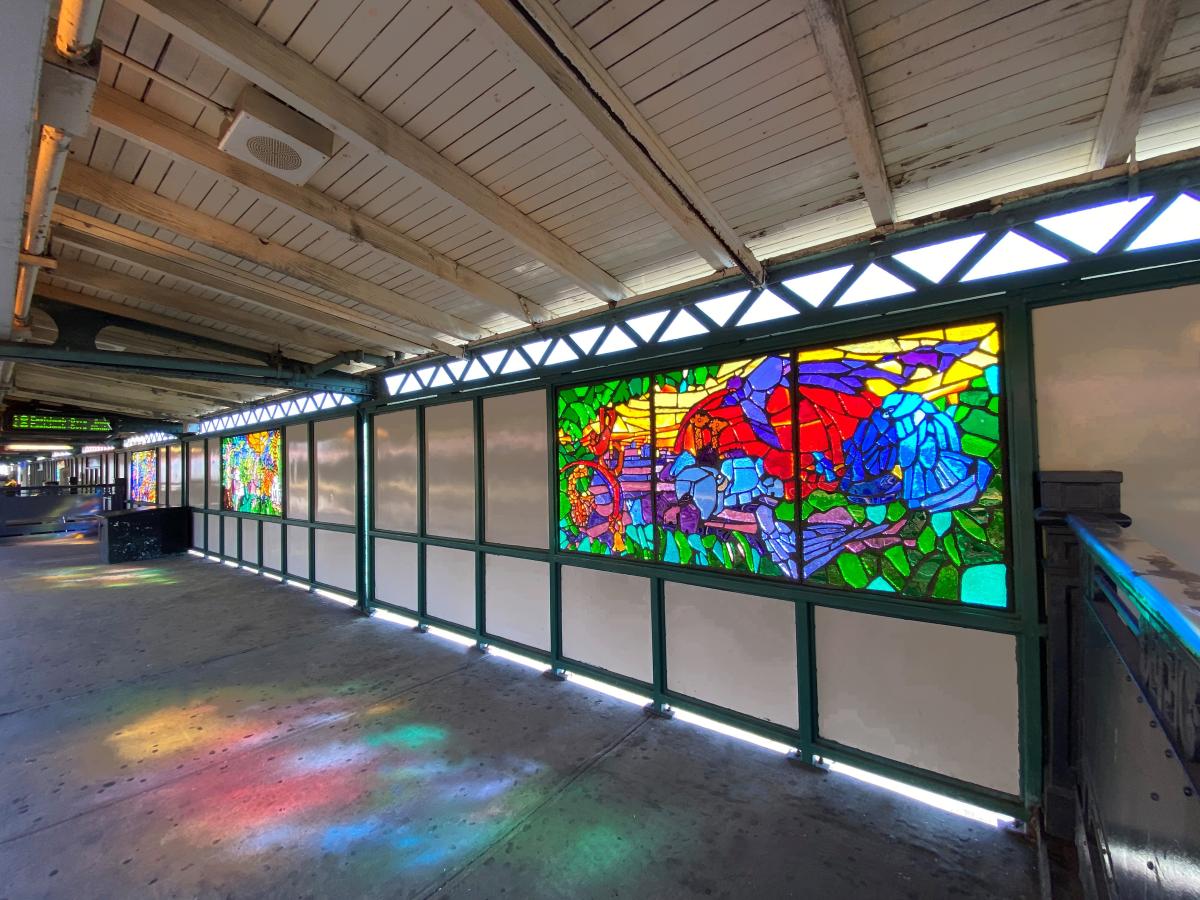 Artwork in faceted glass by Naomi Campbell showing colorful animals in a lush setting in platform windscreens. 