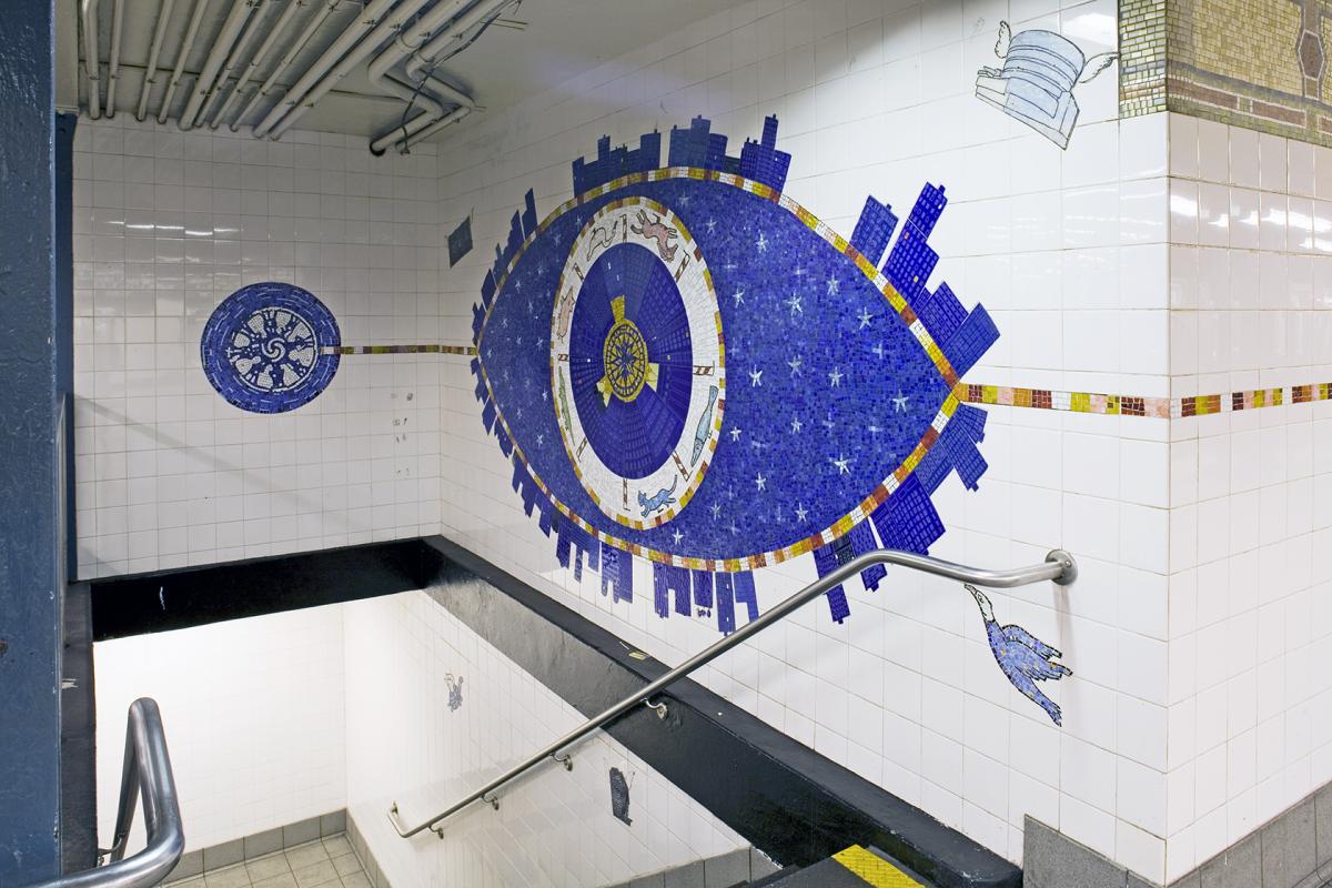 Artwork in glass mosaics and etched stone by Peter Sis showing four large eyes in bold colors, above the stairs, with pupils and eyelashes drawn with buildings and people. 