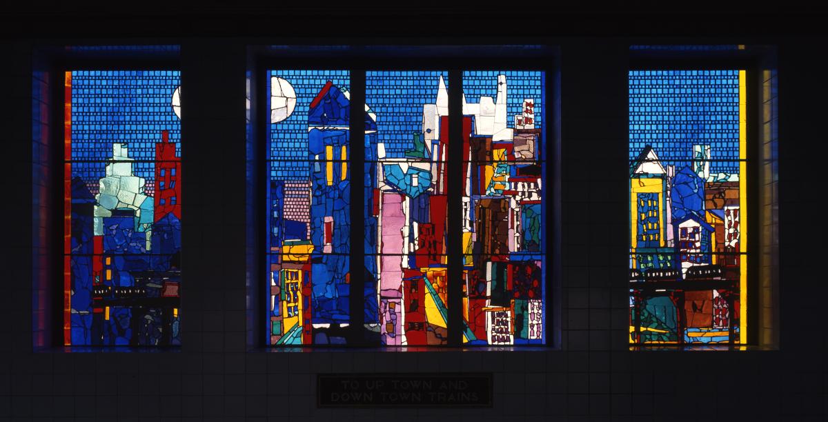 Artwork in Faceted glass by Romare Bearden showing a colorful cityscape with a blue background over the stairway.