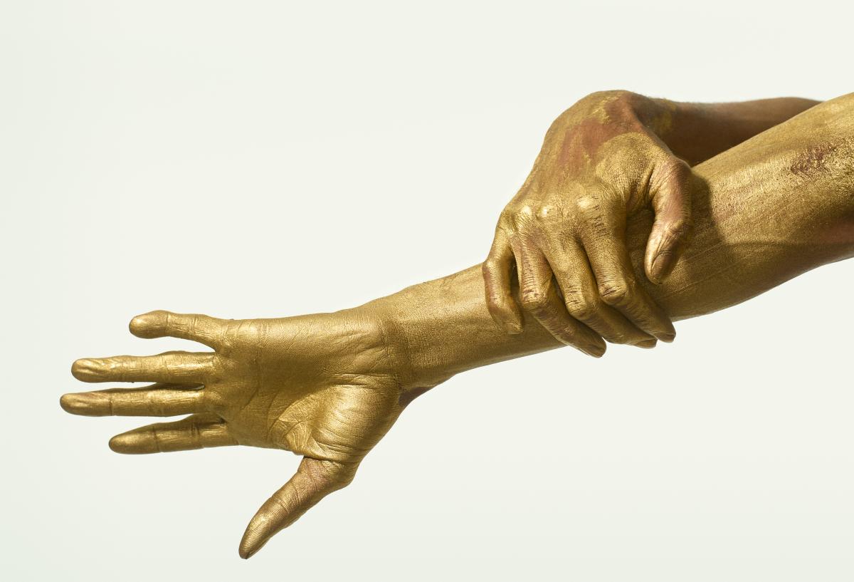 A photograph of a two hands coated in gold paint
