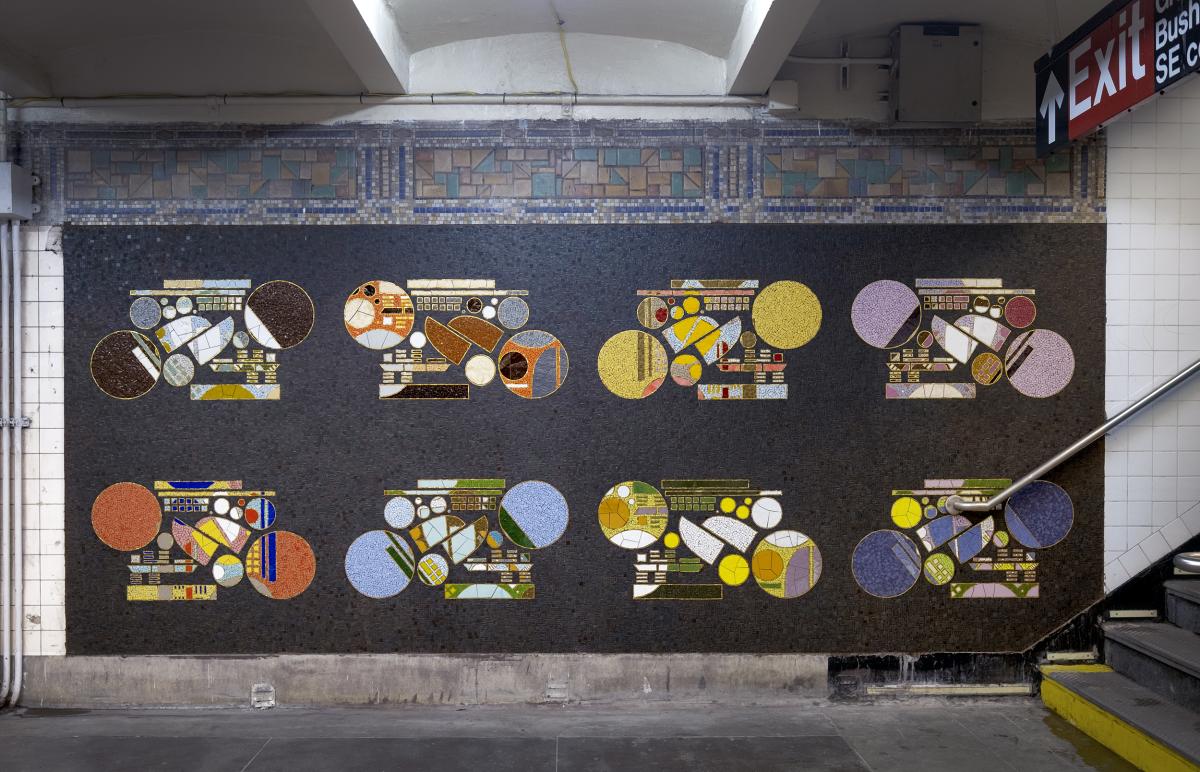 Artwork in ceramic mosaic by Glendalys Medina showing colorful geometric forms against a dark background along the platform wall.