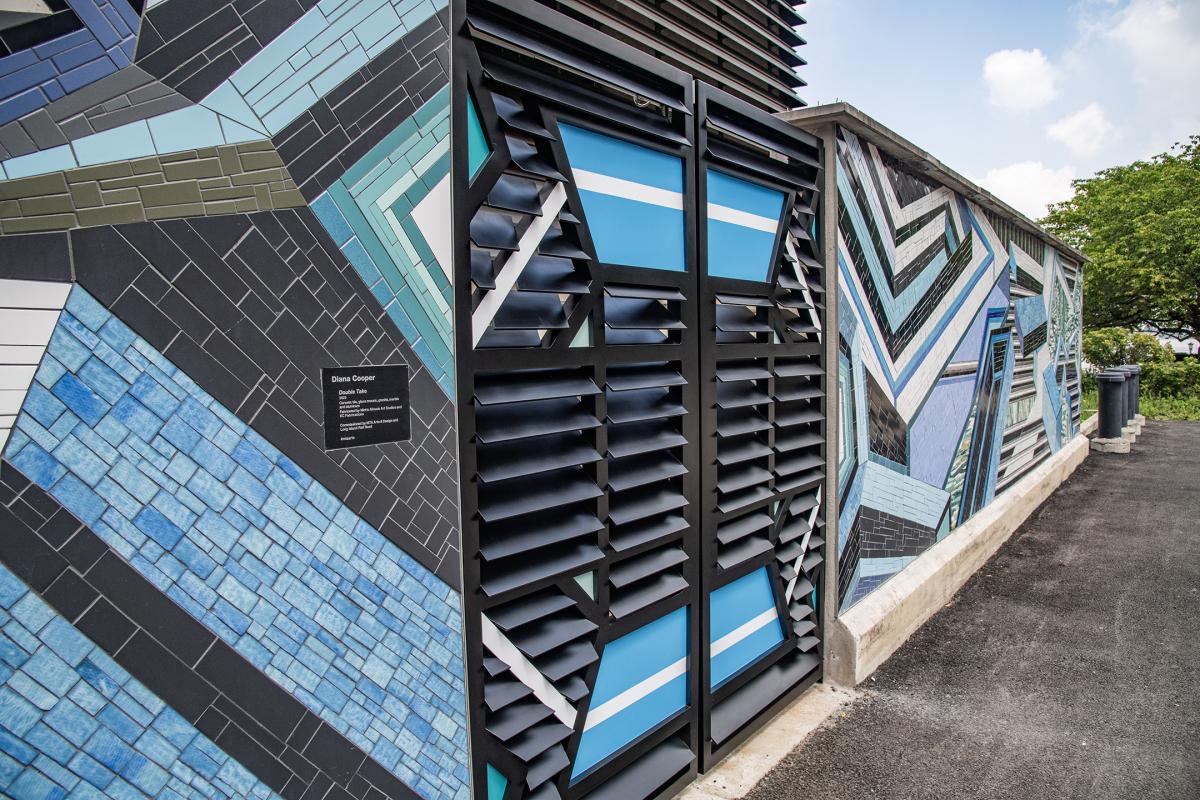 Three-quarters view of mosaic artwork and designed metal gate featuring a blue, gray, white, and black geometric design.