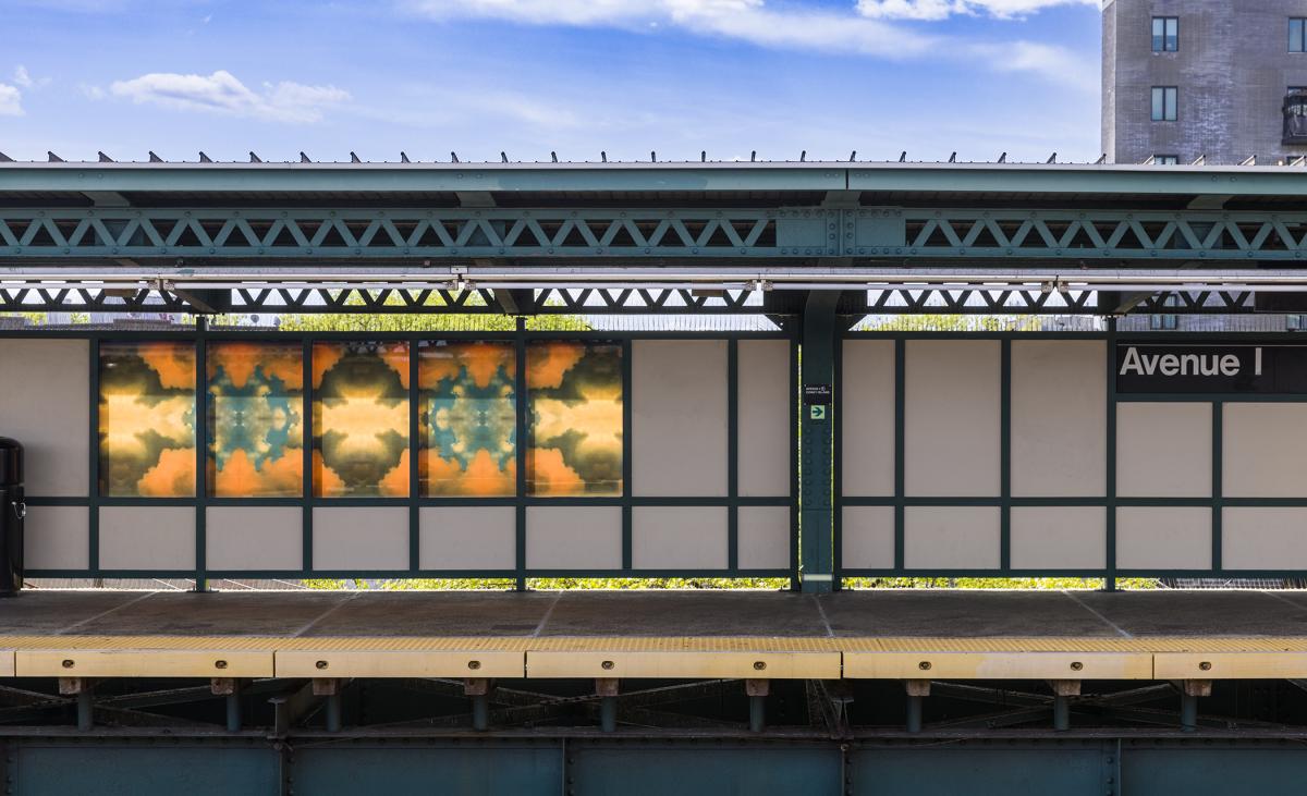 Glass artwork on an elevated station platform depicting kaleidoscopic images of clouds.