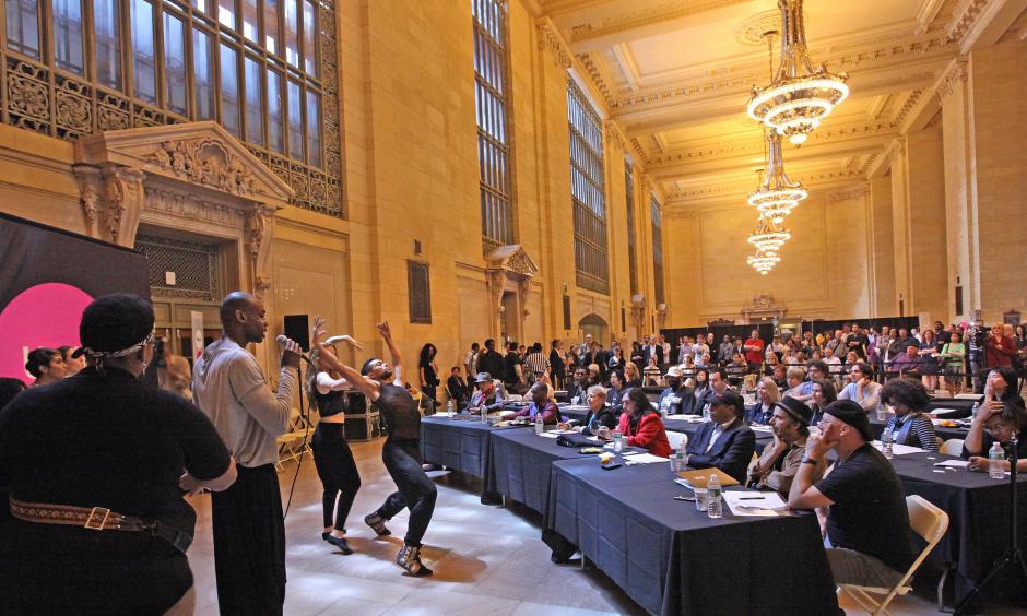 Performers sing and dance in front of a large panel of people at Grand Central Terminal 