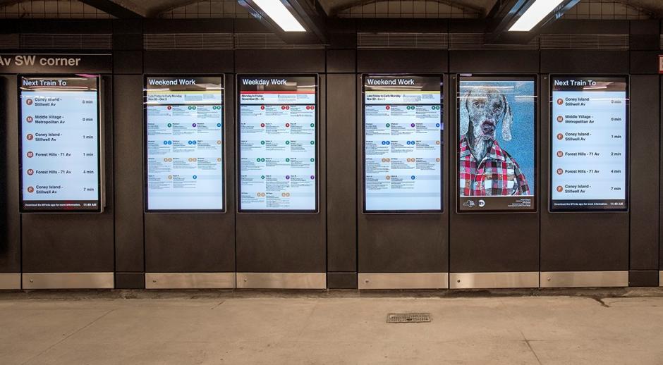 Digital screens on a subway platform show a subway map, details about weekend work, the next train to arrive and a piece of artwork (a mosaic of a dog in a button-down).
