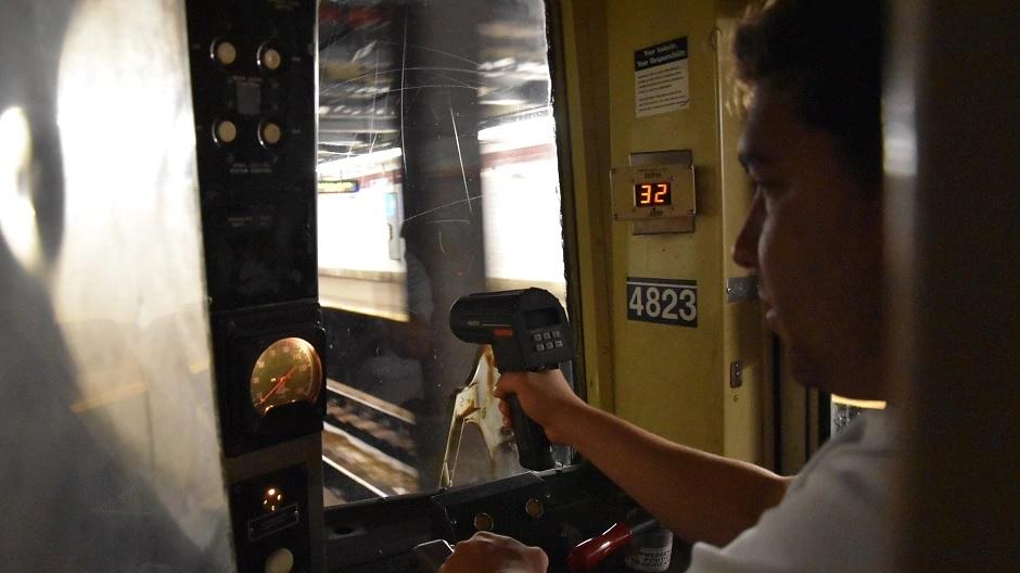 A train conductor uses a speed gun from inside a subway car.