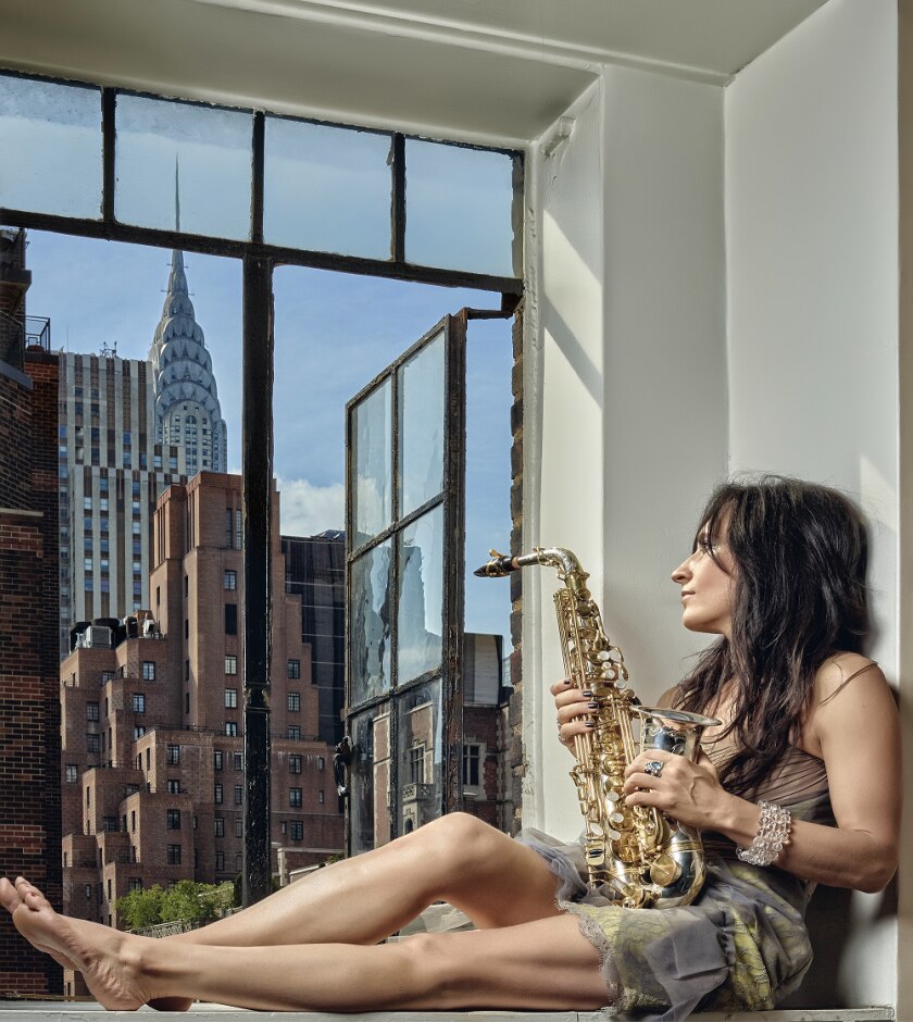 Woman sitting in window sill holding Alto Saxophone.