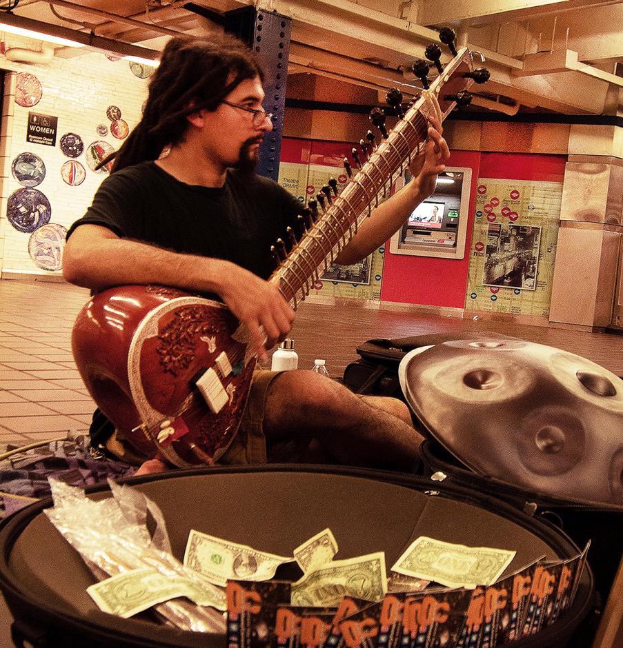 Man playing Sitar in front of tip bucket.
