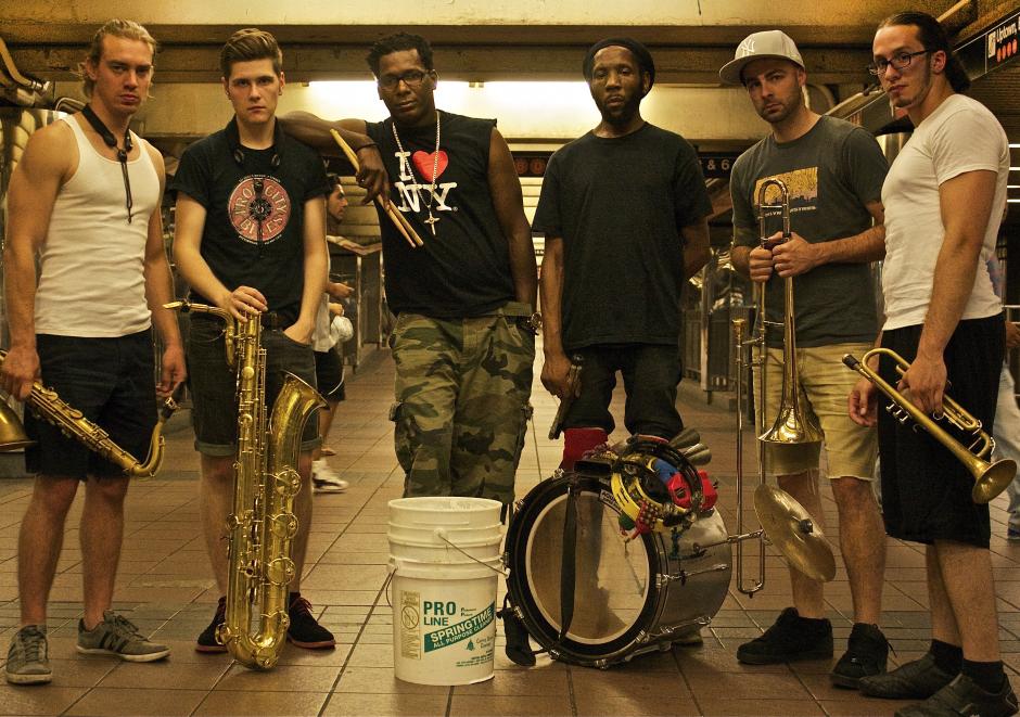  Alt Text 1:   Six men posing for the camera with drums, buckets and saxophone and brass.