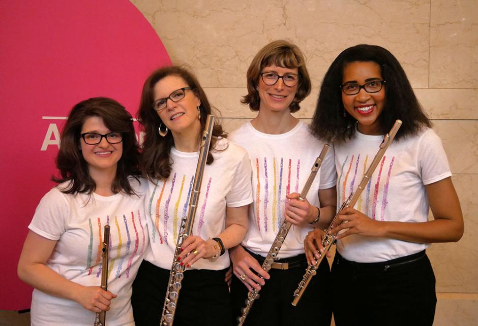 Four women in white tee shirts holding flutes.