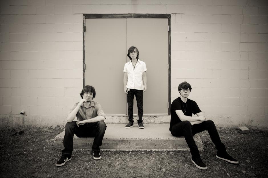 Black and white photo of three teenage boys posing in front of a door.
