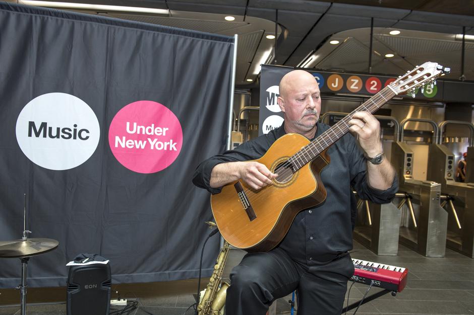 Man playing acoustic guitar in front of music sign.