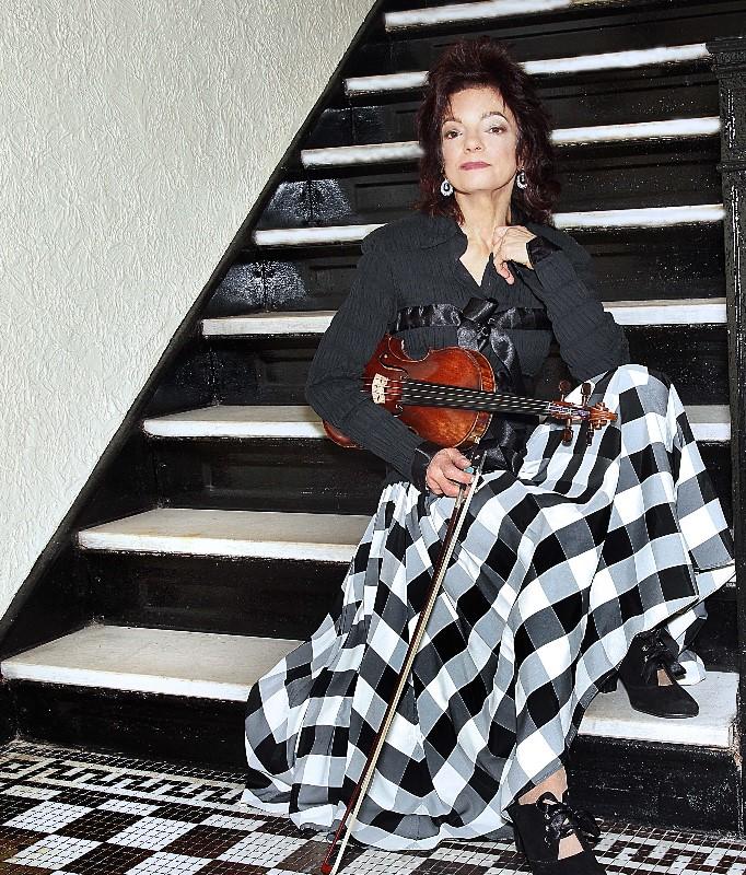 Woman wearing black and white dress sitting on stairs holding violin.