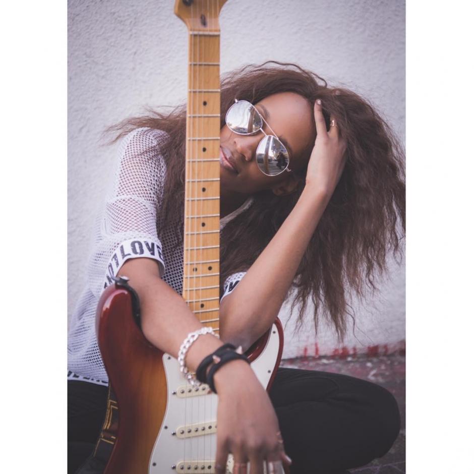 Woman posing wearing sunglasses holding electric guitar.