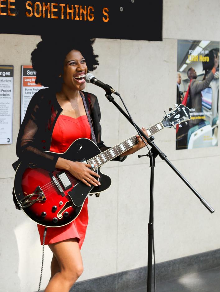 Woman in a red dress playing electric guitar in front of a microphone.