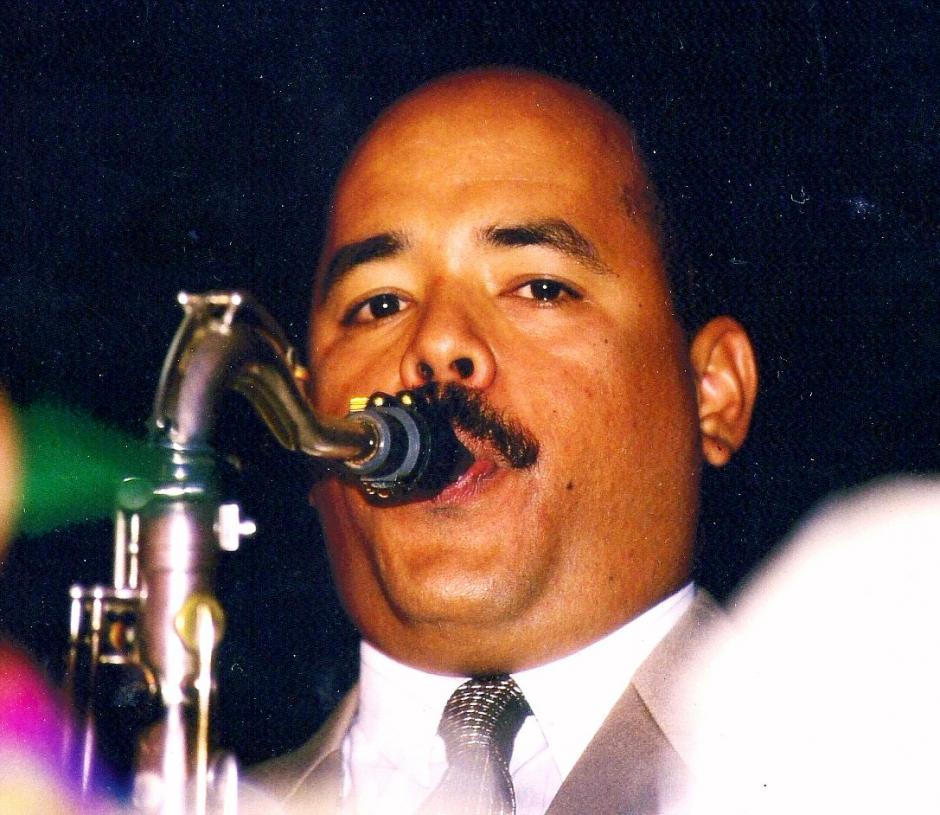 Man in suit and tie playing saxophone.
