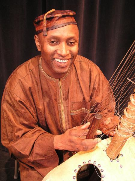 Man in traditional brown suit and hat playing kora.
