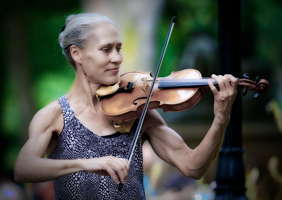 Woman in the park wearing tank top playing violin.