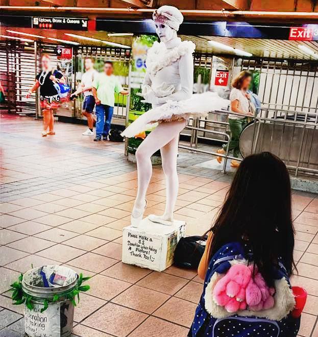 Woman dressed in all white Ballerina outfit in front of tip bucket.