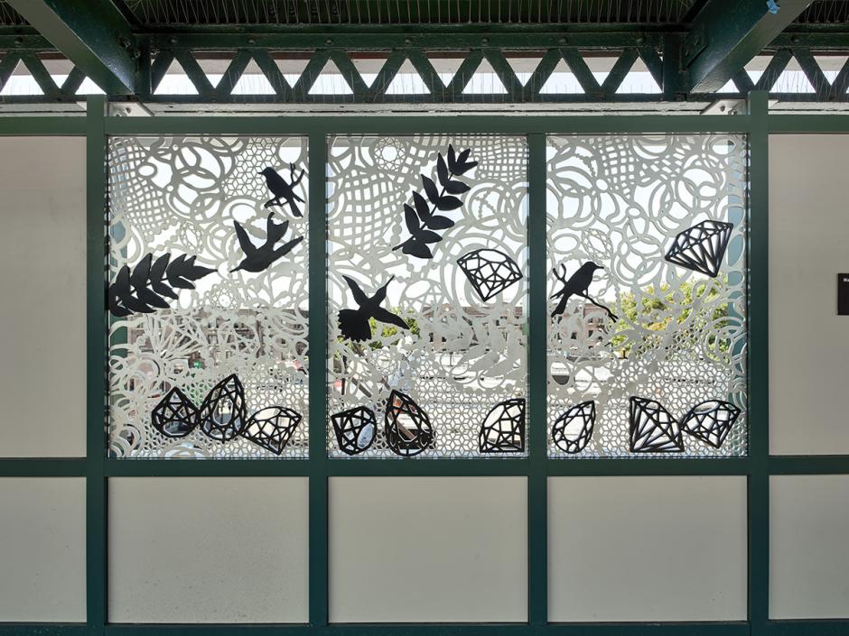 Metalwork window by Nancy Baker showing black birds, ferns, and gemstones in front of white lacework.
