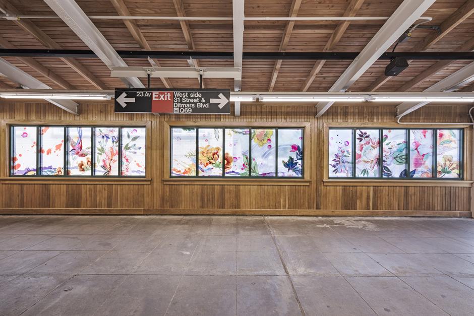 Photograph of station mezzanine interior with a straight on view of laminated glass artwork panels. Panels feature painterly flowers, brush strokes and birds. 